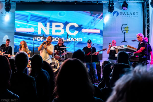 NBC auf der Bühne mit Publikum davor.